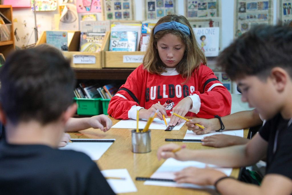 A student in a red sweatshirt using a ruler to draw grid lines on paper.