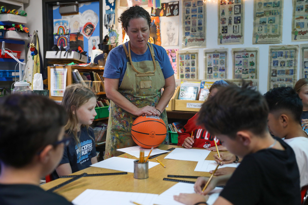 An art teacher demonstrating 3D shading techniques using a basketball as a visual aid.