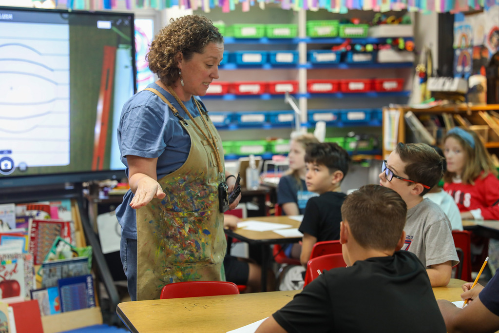 An art teacher gesturing while explaining a lesson to her seated students.