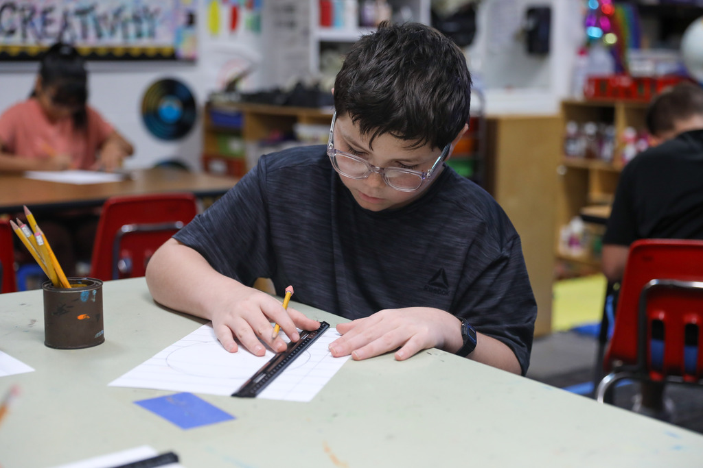 A student using a ruler and pencil to construct precise lines on paper during art class.