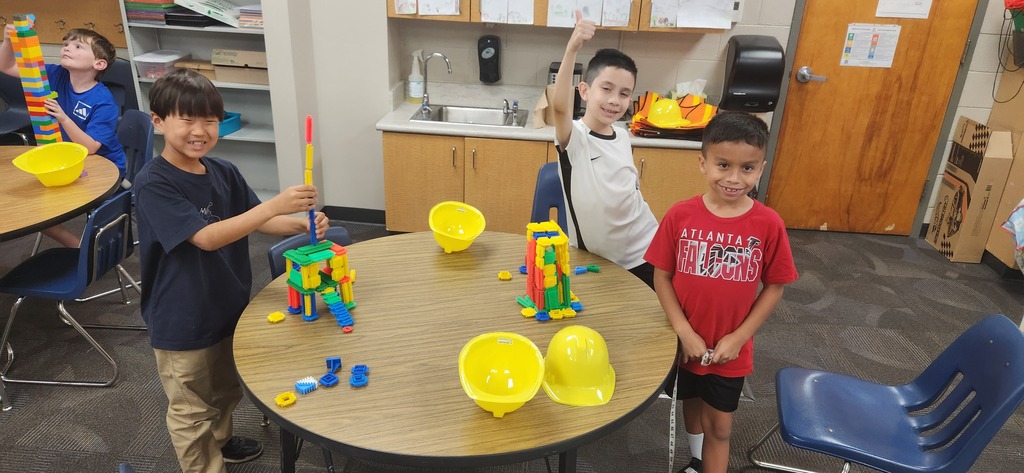 students smiling at a table in a classroom while using blocks and magnet tiles to experience a day on the job of a construction worker!
