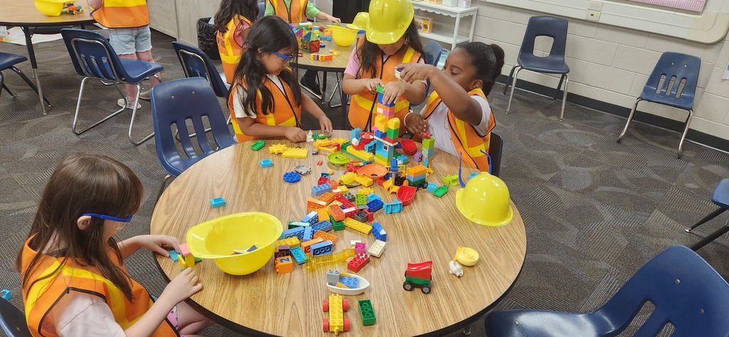 students smiling at a table in a classroom while using blocks and magnet tiles to experience a day on the job of a construction worker!