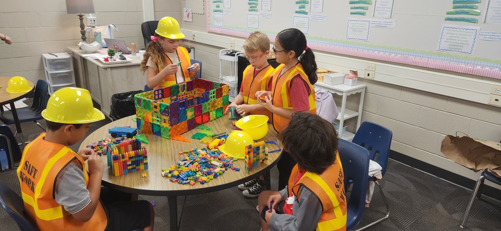 students smiling at a table in a classroom while using blocks and magnet tiles to experience a day on the job of a construction worker!