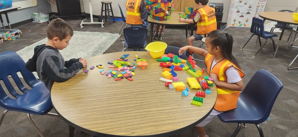 students smiling at a table in a classroom while using blocks and magnet tiles to experience a day on the job of a construction worker!