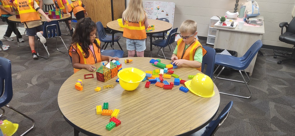 students smiling at a table in a classroom while using blocks and magnet tiles to experience a day on the job of a construction worker!