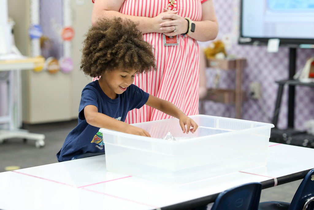 A young student testing his aluminum foil boat design in a water bin.