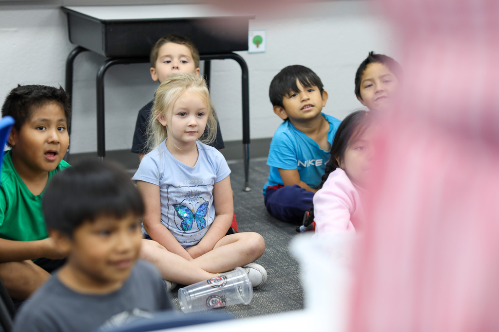 Primary students sitting cross-legged on the carpet listening during a classroom experiment.