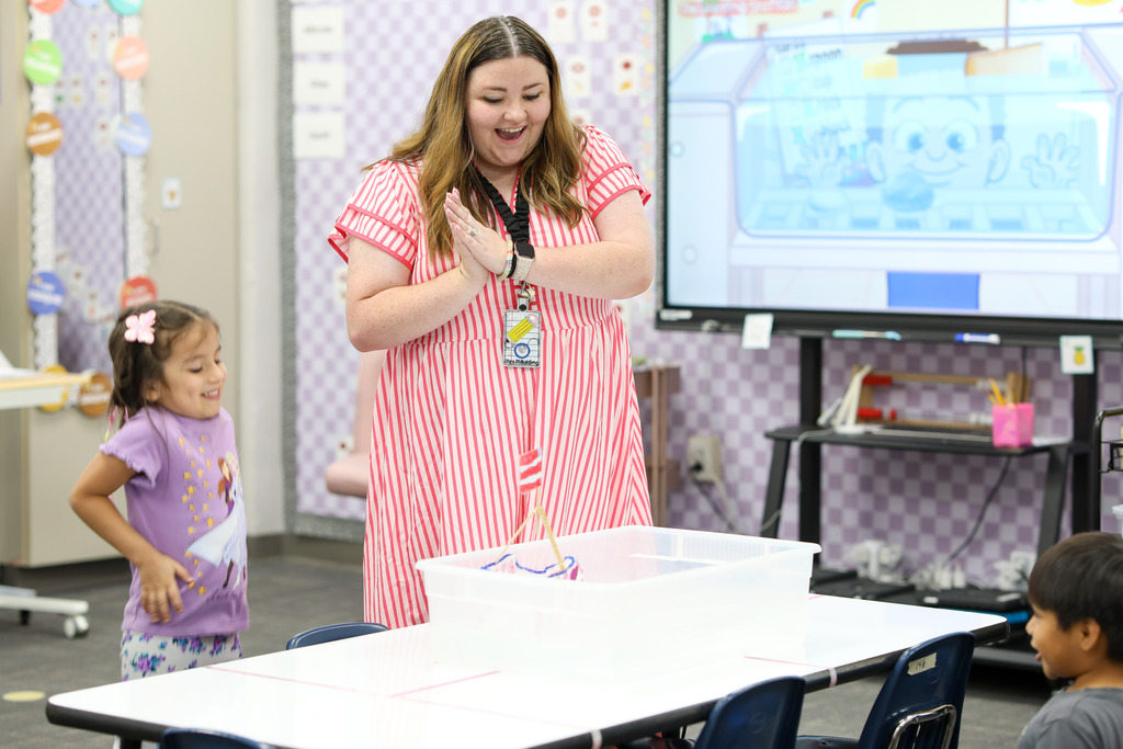 A teacher applauding a student as her handmade boat floats successfully.