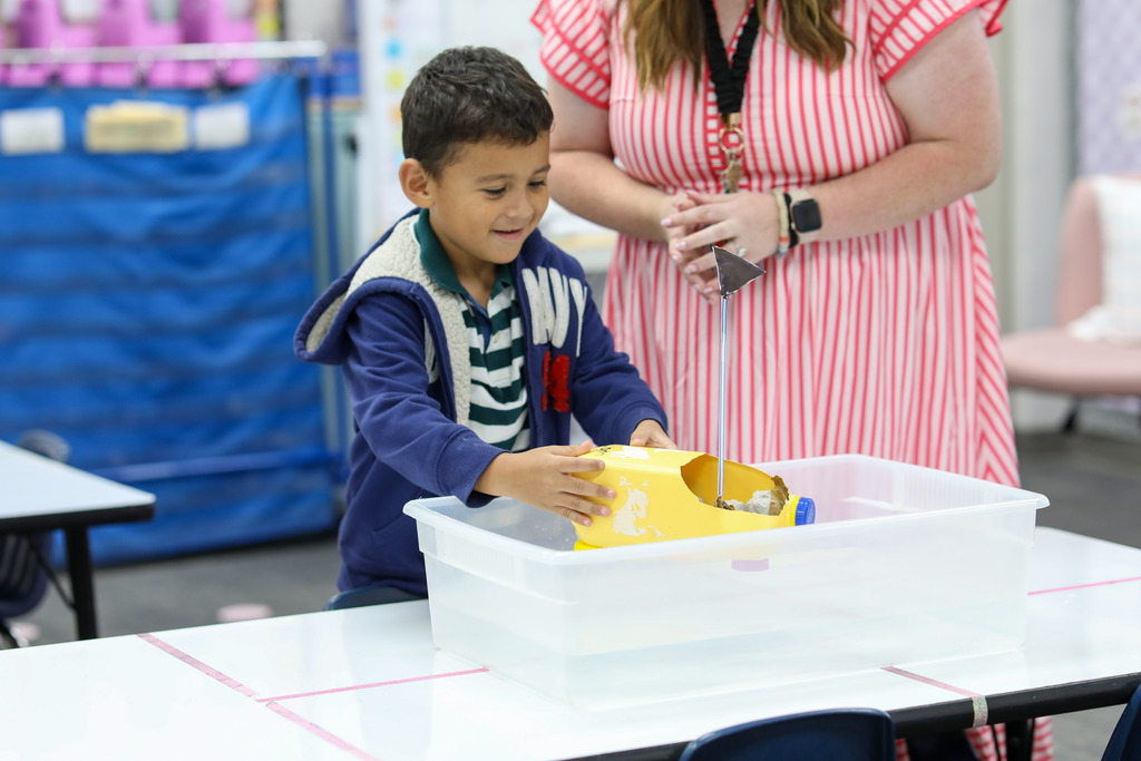 A student placing a recycled plastic jug boat into a water tub.