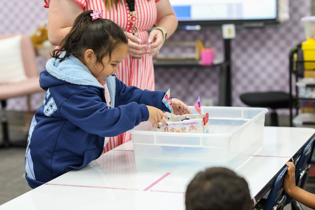 A young student carefully placing her decorated toy boat into a water container.