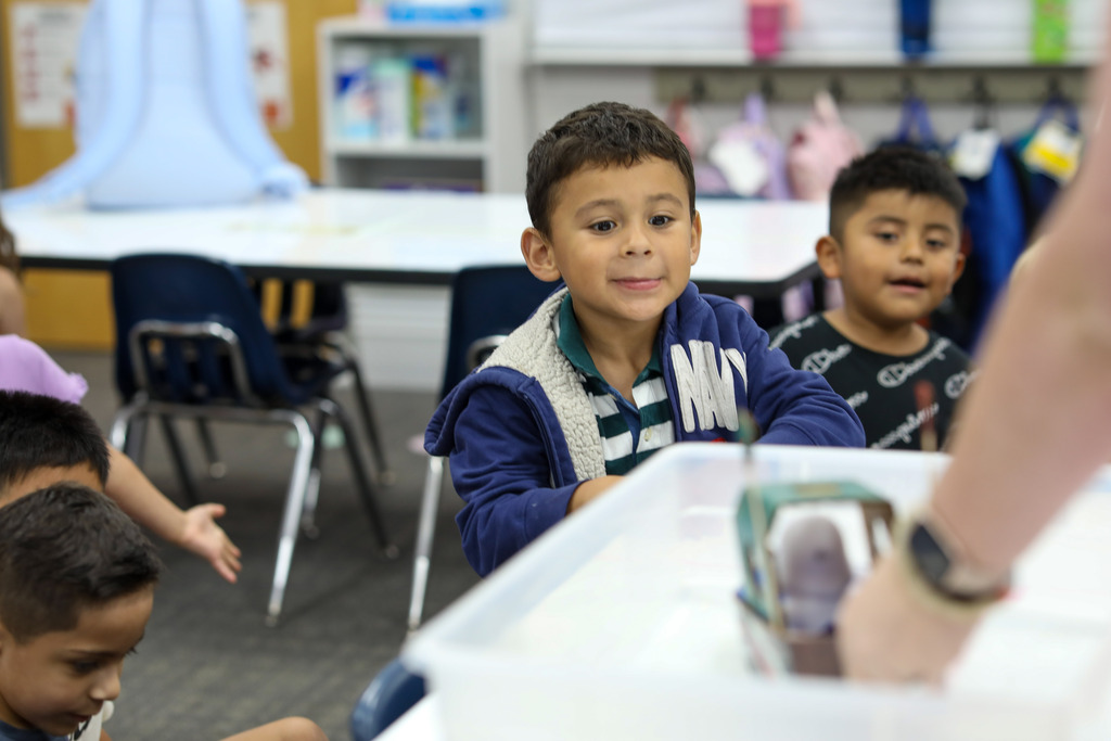 A young student watching intently as a teacher places a toy boat in a water tub during a buoyancy lesson.