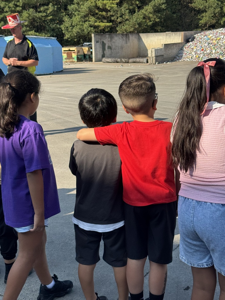 two students hugging while listening to a landfill worker talk
