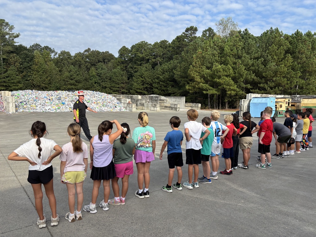 students standing in a line listening to a landfill worker talk to them about recyling in front of a large pile of cans