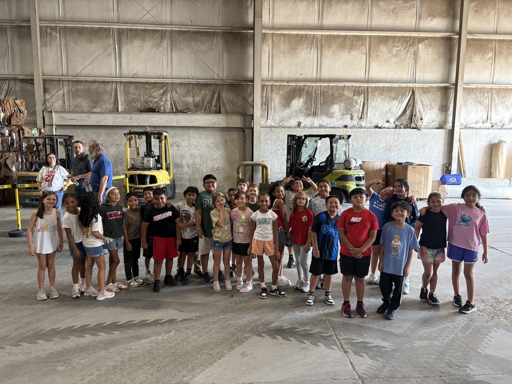 a class of students standing and smiling for a picture inside the recycling facility