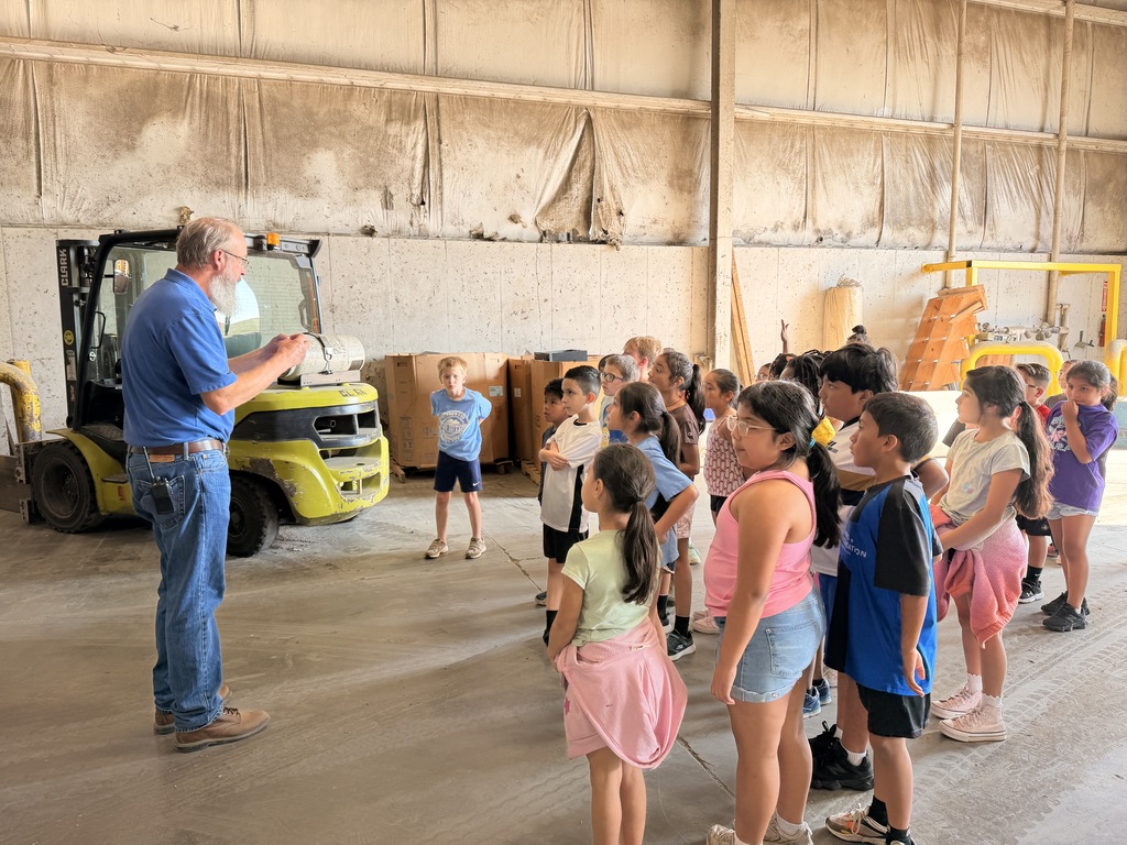 students in a group inside of the recycling facility listening to a worker share about his career while in front of a forklift