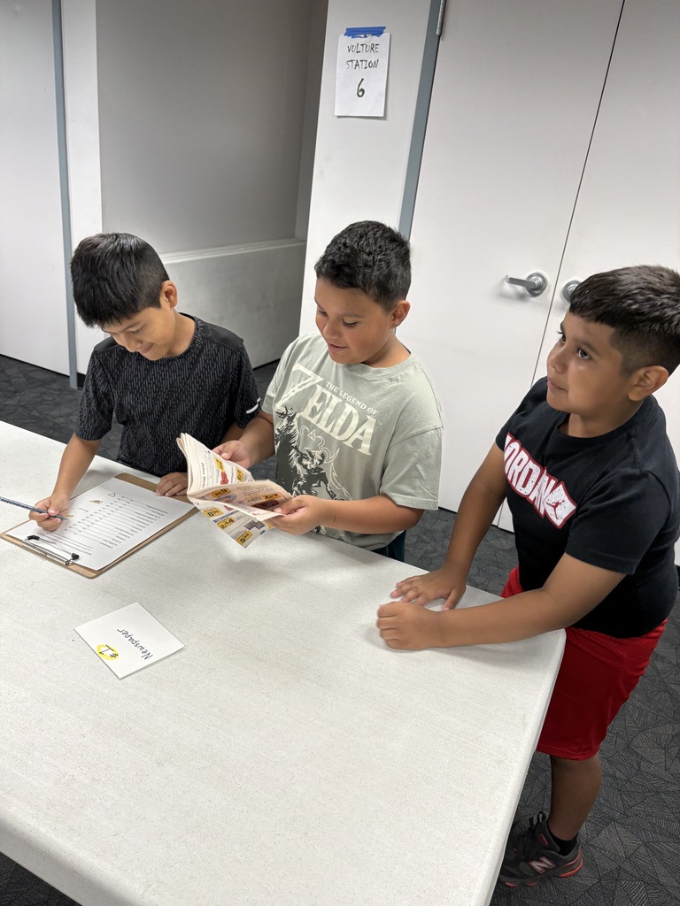 students working together in a group to complete an activity about recycling. They are standing together at a table while holding papers and pencils