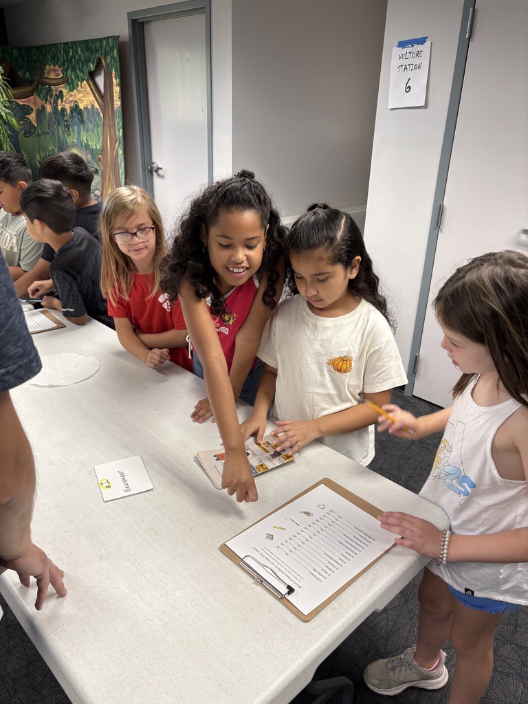students working together in a group to complete an activity about recycling. They are standing together at a table while pointing to information they learned from their fieldtrip