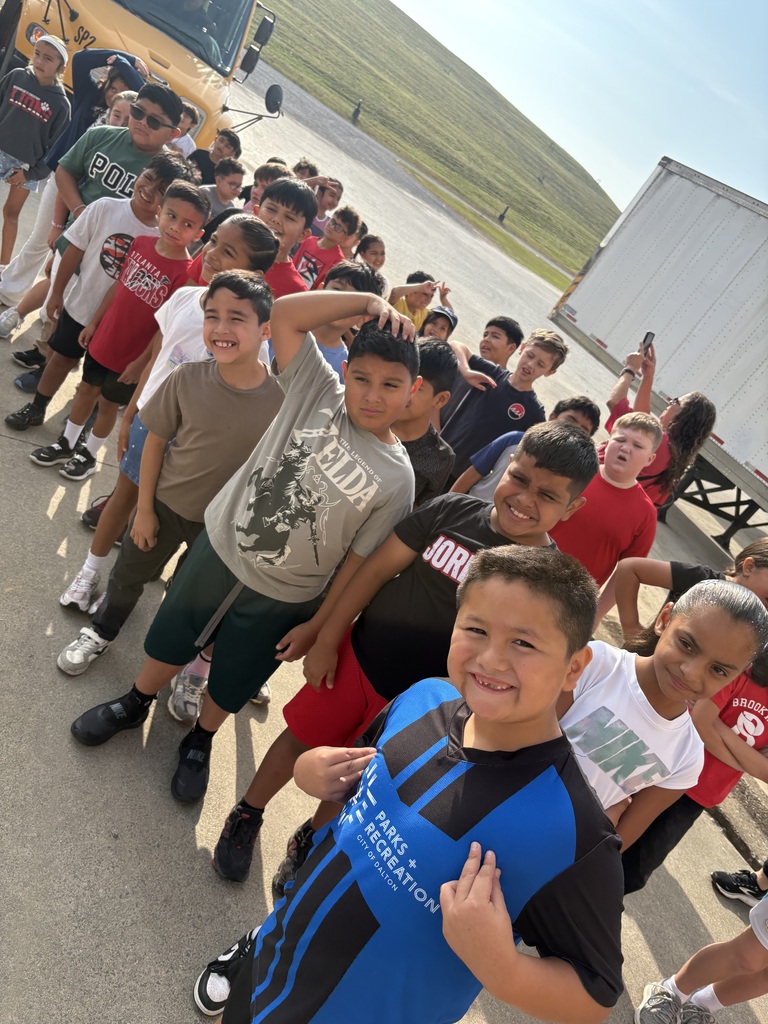 students standing outside of a bus on a pretty day smiling for the camera as they wait to begin their field trip to the landfill