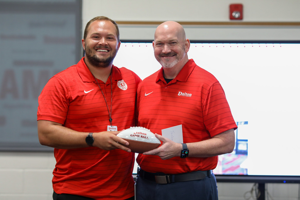 Dr. Steven Craft presenting a Dalton Game Ball football award to a male staff recipient.