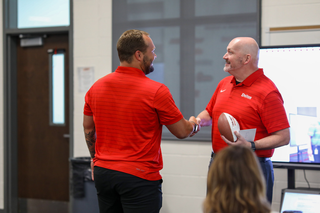 Superintendent Dr. Steven Craft shaking hands with a male staff member while holding a Game Ball award.