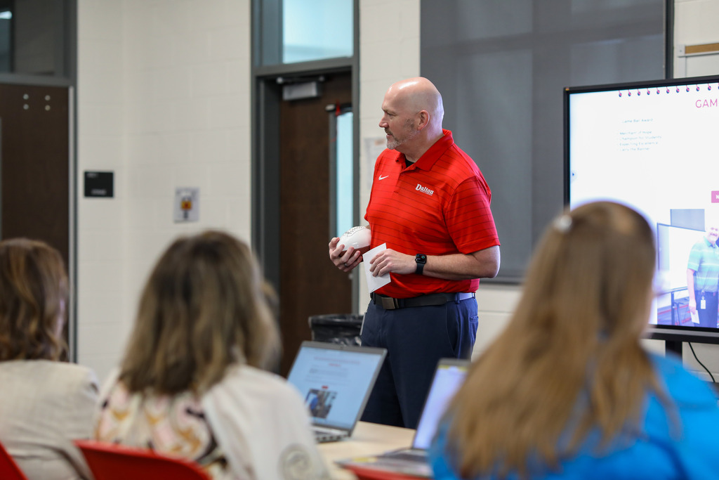 Dr. Steven Craft addressing a room of staff members while holding a Game Ball award.