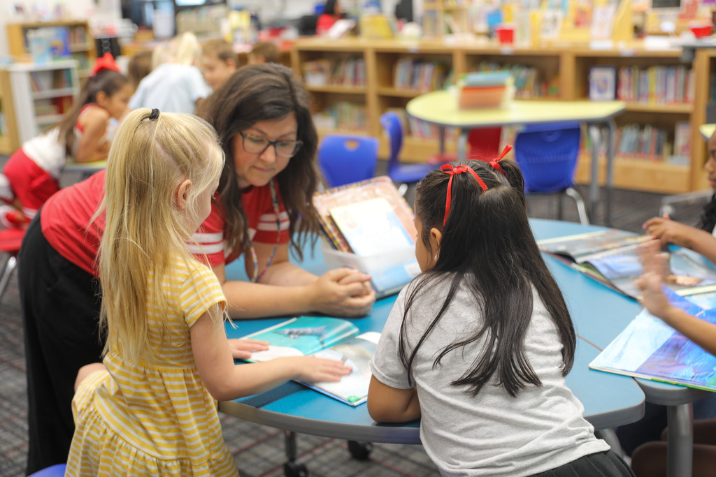 A librarian leaning over a blue table helping students with their reading choices.