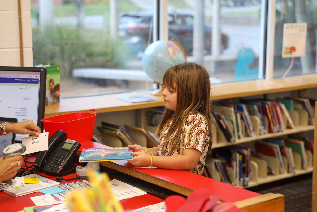 A young student checking out a library book at the circulation desk.