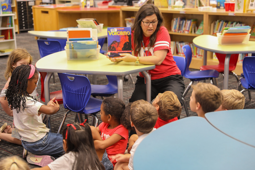 A media specialist holding up a book about volcanoes during storytime.
