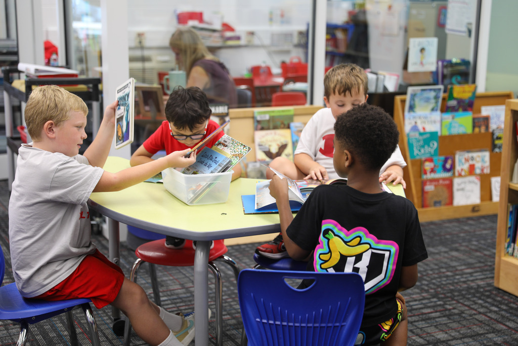 Four students sitting around a green library table reviewing books together.