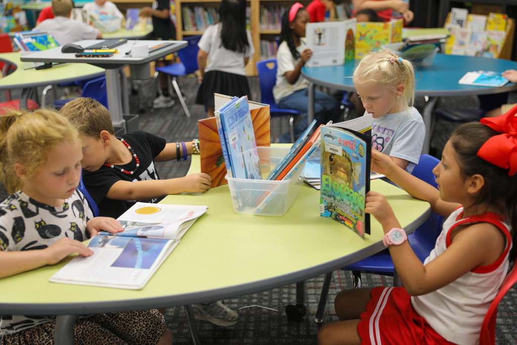 Students gathered around a light green activity table reading library books.