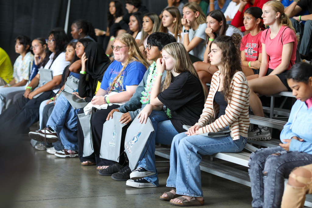 High school students seated on bleachers listening attentively to a presentation.