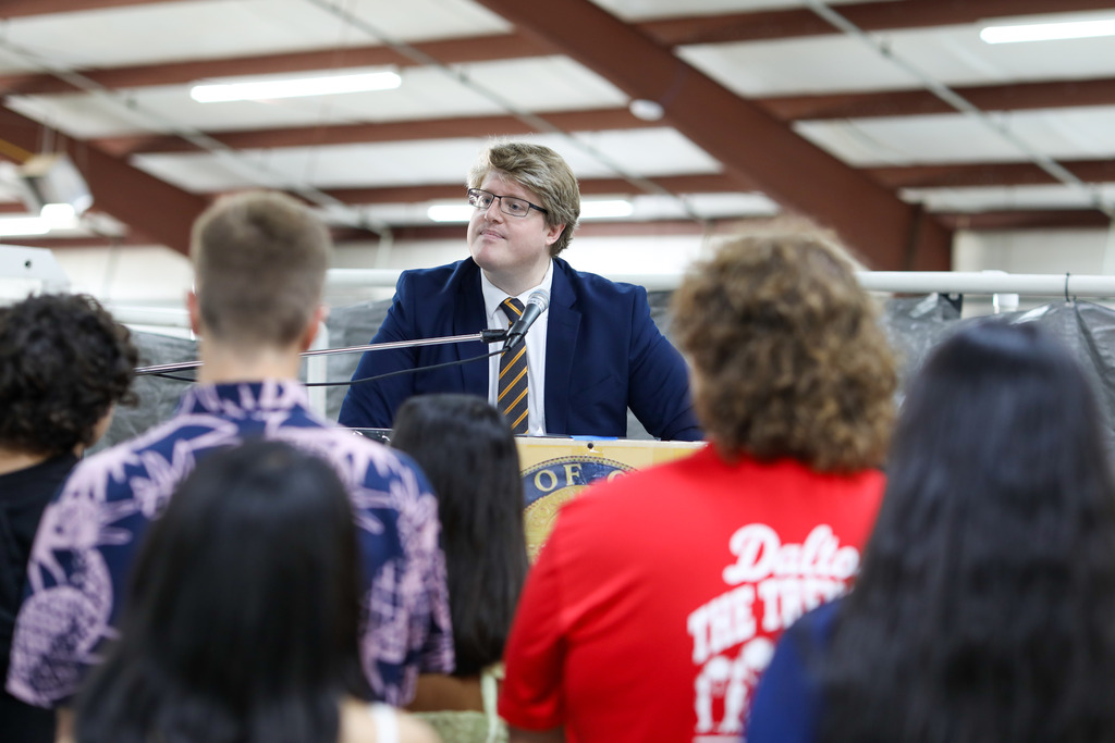 A guest speaker in a suit speaking from a podium to a group of gathered students.