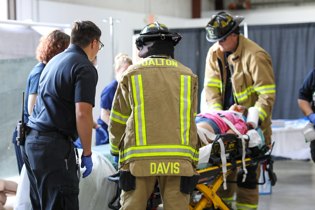 Emergency responders demonstrating first-aid and patient transport techniques to students.