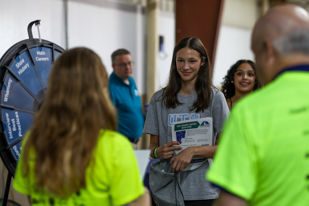 A student holding informational pamphlets while standing at an interactive prize wheel during a career fair.
