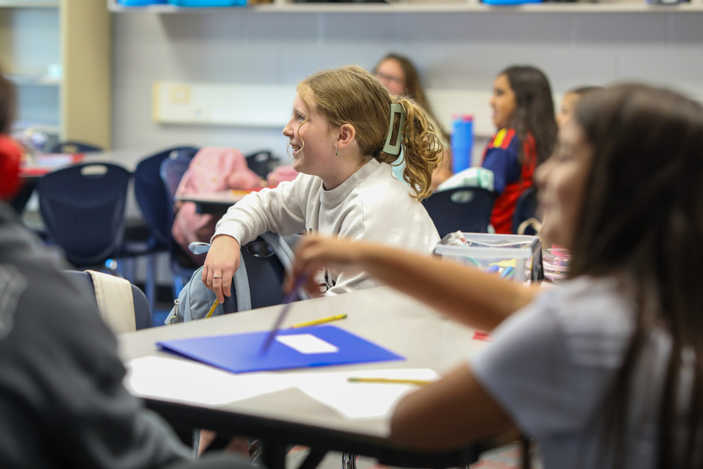 A student smiling at her desk while participating in a group discussion.