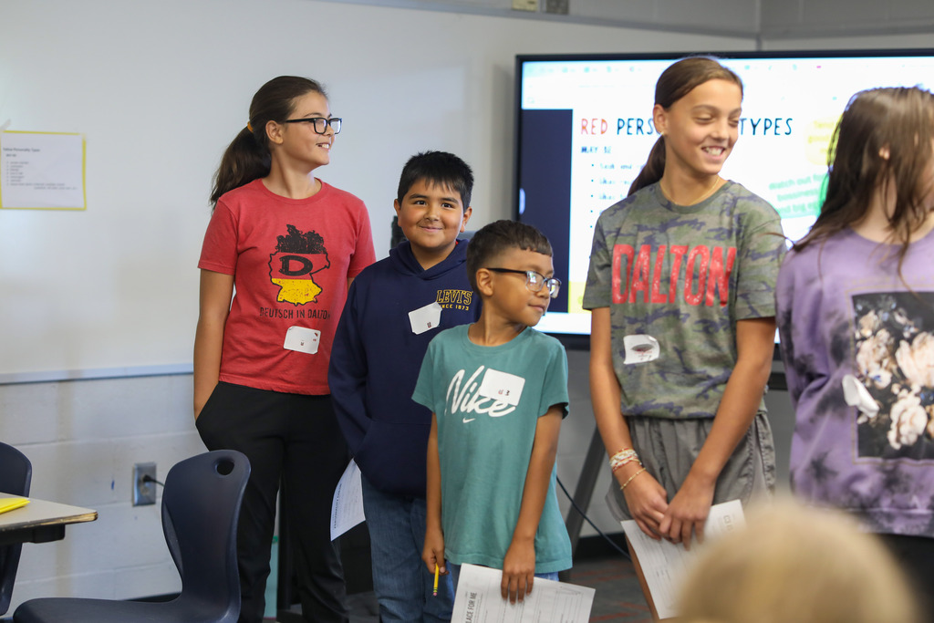 A group of students standing near a digital board sharing their work.