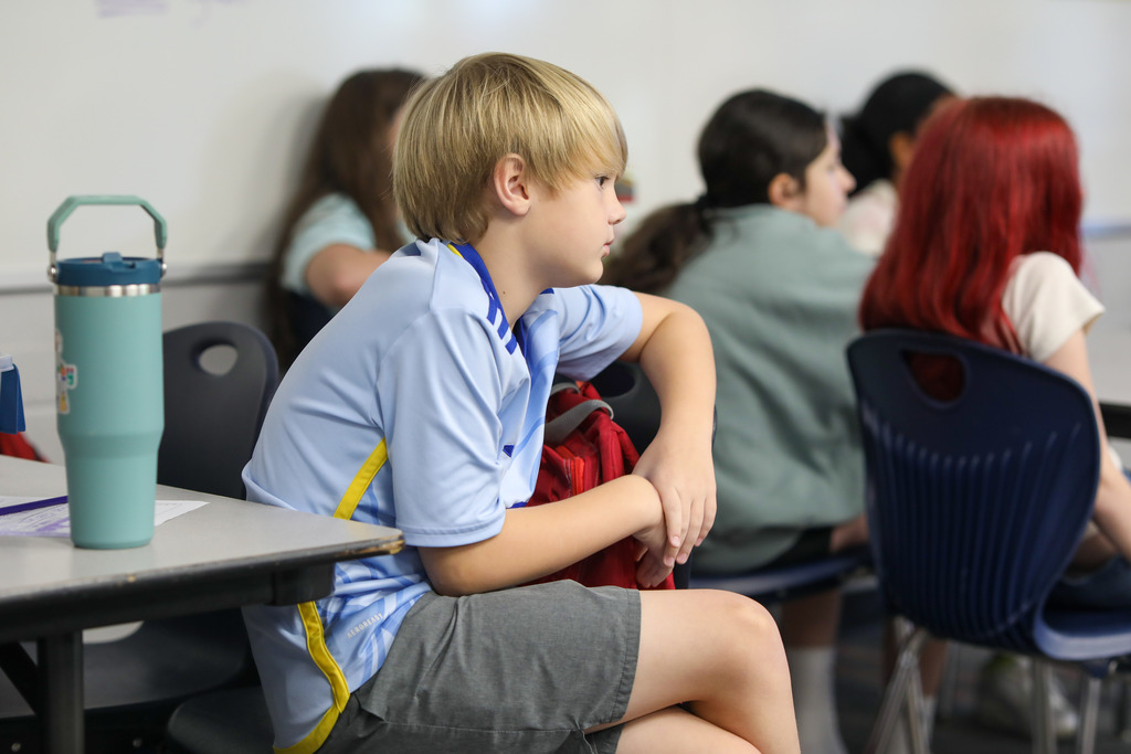 A student seated at his desk attentively watching a teacher's presentation.