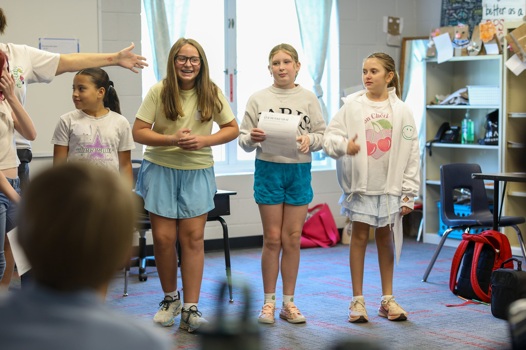 Four students standing at the front of the room presenting a project to classmates.