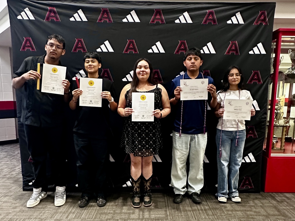 Group photograph of newly inducted French and Spanish Honor Society members holding certificates and candles in front of an Adidas logo backdrop.