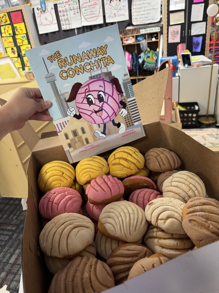 A hand holds a copy of The Runaway Conchita above a box filled with colorful traditional Mexican conchas in a classroom.