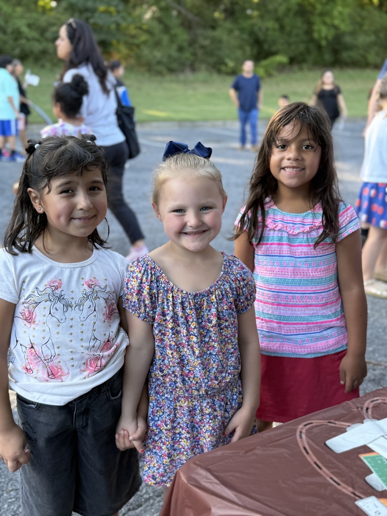 three students posing and smiling while visiting a table at literacy night outside!