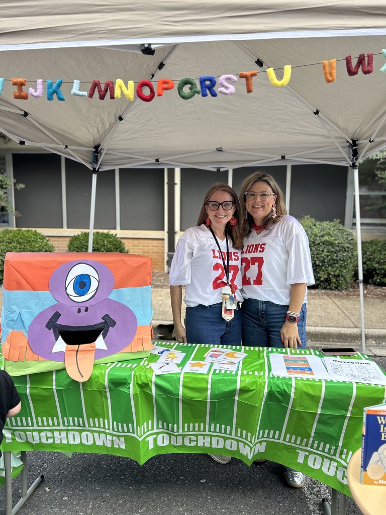 two teachers smiling and dressed in brookwood football jerseys standing in front of their Pre-K tent at Literacy night