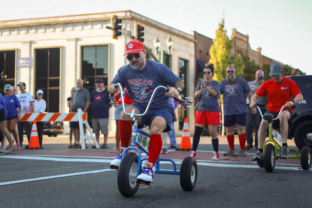 A participant riding a blue tricycle in a street race while spectators cheer.