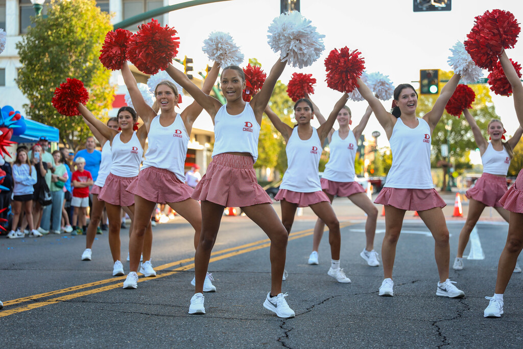 Cheerleaders in red gingham skirts performing a synchronized routine on the street during a community parade.