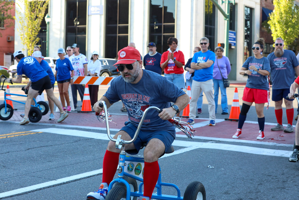 A tricycle race participant navigating a downtown street course as crowds look on.