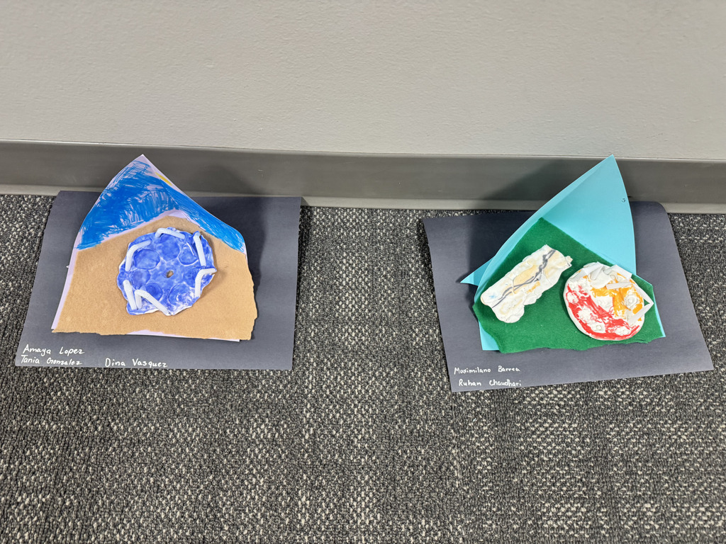 Two student-designed playground models displayed on black construction paper. Students used felt, paper, clay, and other craft materials to demonstrate their ideas for improving playground safety.
