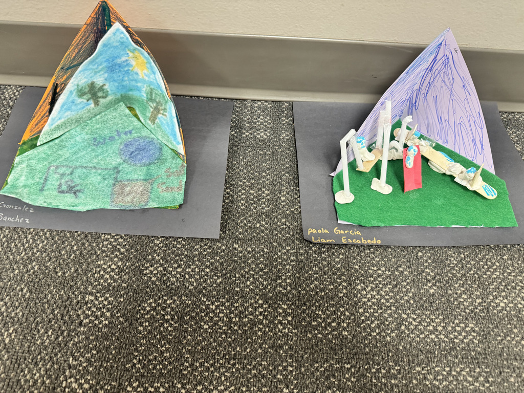 Two colorful third-grade student-created 3D models showing ideas for safer playgrounds. The models use paper, felt, craft sticks, clay, and other materials to represent playground equipment and outdoor spaces.