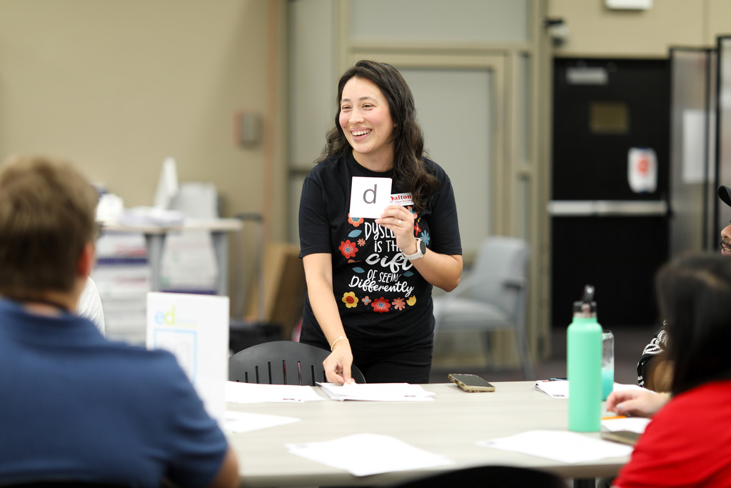 An instructional coach holding a card with the letter d on it.