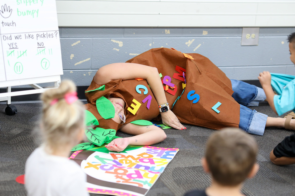 A teacher lays on the ground dressed as a tree.