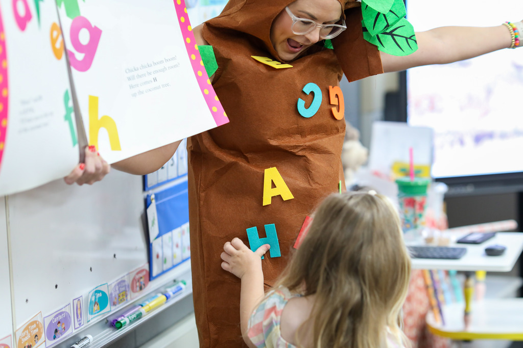 A student places a letter on the teacher dress as a tree.